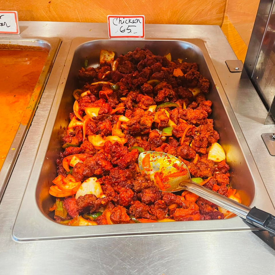 A buffet tray of Indian Chicken 65, featuring red-spiced chicken pieces with onions and peppers.
