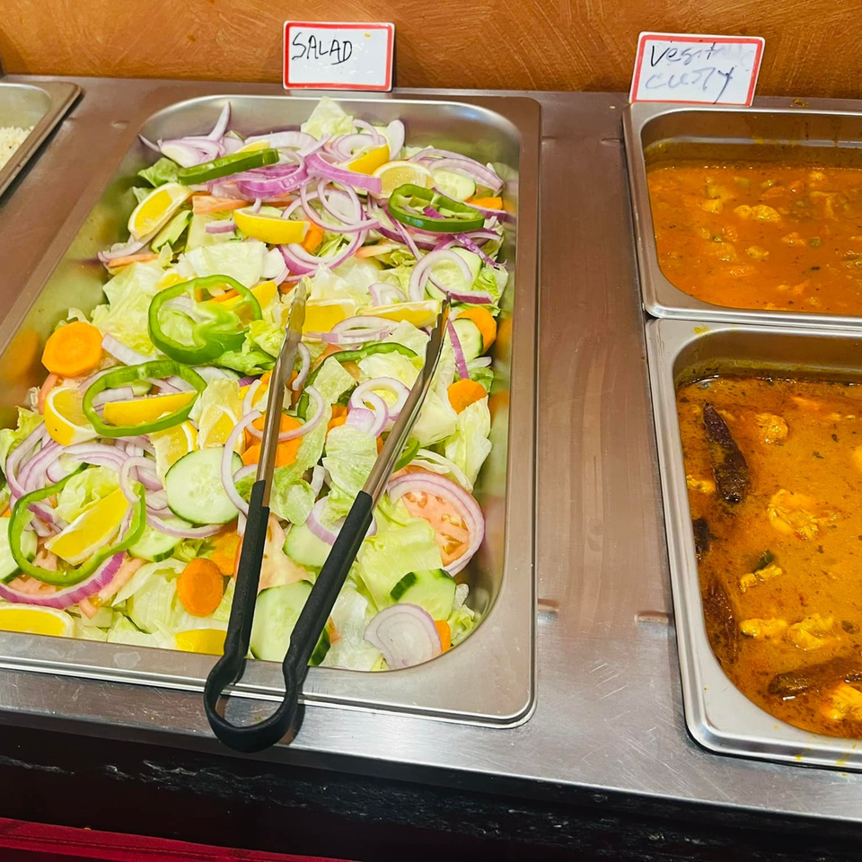 A buffet spread with a fresh salad and two trays of Indian vegetable curry.