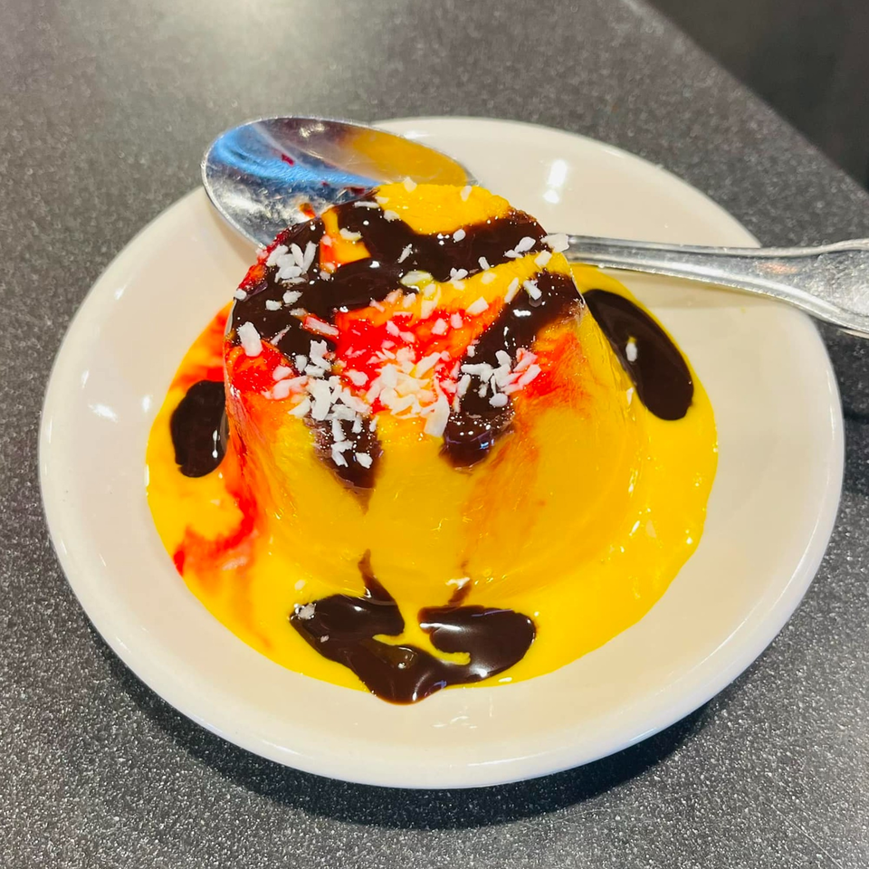 A vibrant Indian mango pudding dessert, drizzled with chocolate and sprinkled with coconut flakes.